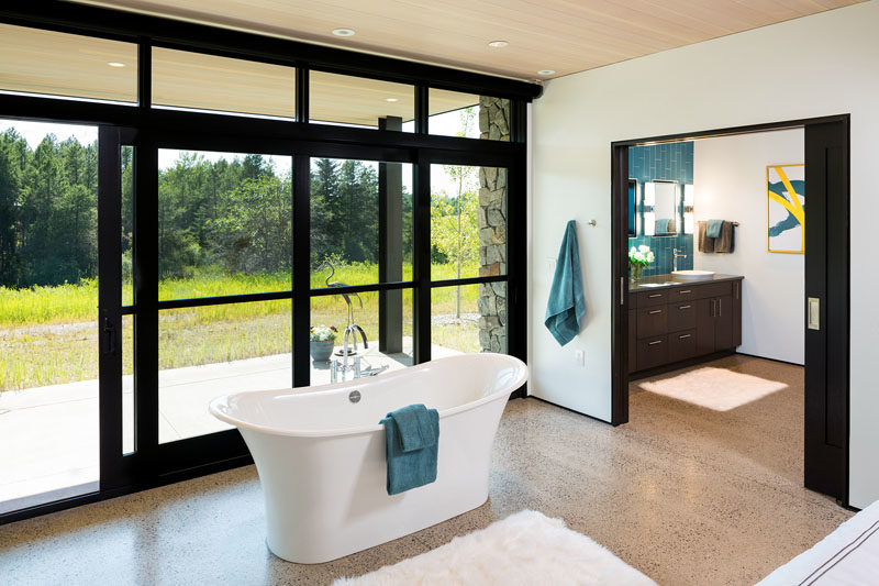 In this modern bedroom, a freestanding bathtub takes center-stage, with it positioned in front of the windows.  #FreestandingBathtub