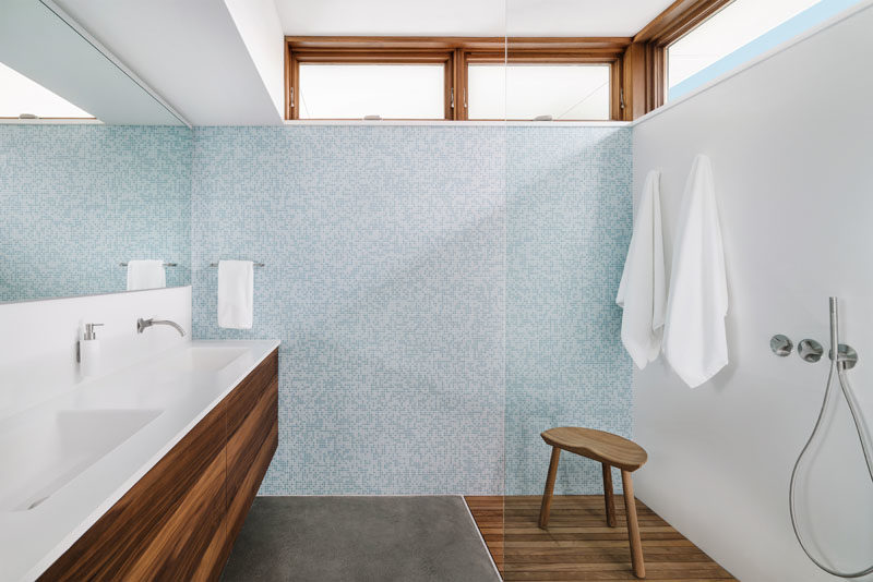 Bathroom Ideas - In this modern bathroom, a minimalist wood vanity with integrated sinks lines the wall, while a tiled wall adds a soft touch of color, and clerestory windows allow natural light to filter through. #BathroomIdeas #VanityIdeas #ModernBathroom