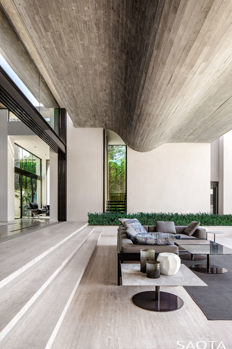 The main living areas of this modern house step down to the landscaped terrace. Throughout the home, vein cut Travertine floors have been featured, while the ceiling features a wavy concrete element. #ModernHouse #ConcreteCeiling #TravertineFloors