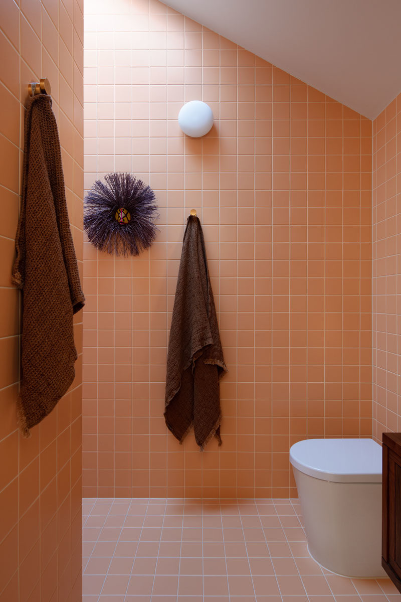 Bathroom Ideas - This modern ensuite bathroom has been covered in peach colored tiles, and features with an angled ceiling. The shower is located around the corner, directly beneath a skylight. #ModernBathroom #BathroomIdea #SquareTiles #PeachTiles #BathroomDesign