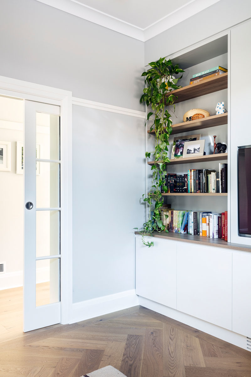 Home Library Ideas - This modern home library has a glass pocket door, while inside, open wood shelving provides a place to show off books and decor, while cabinets below provide additional storage. #HomeLibrary #Playroom #Shelving