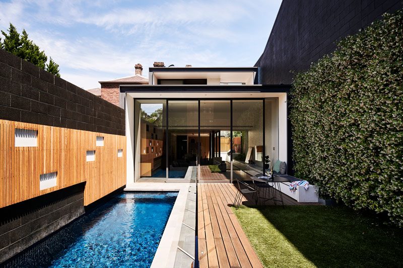 This modern house has sliding glass doors that open the living room to the outdoor space, that features a patio, yard, green wall, and swimming pool. #GlassWall #SwimmingPool #LandscapeDesign