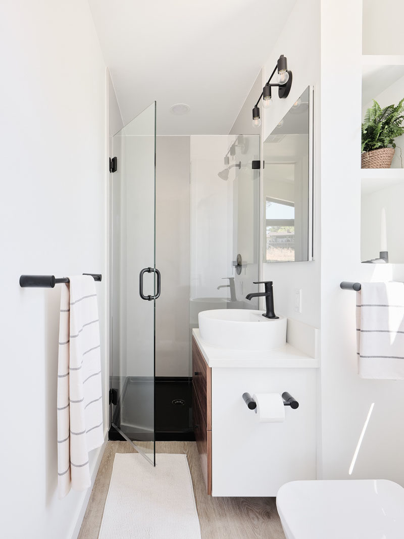 Tiny House Ideas - In the ensuite bathroom of this tiny house, a glass shower door allows light to travel through to the shower, while beside the toilet are built-in shelves. #TinyHouseIdeas #TinyHouseBathroom #ModernBathroom #SmallBathroom #BathroomDesign