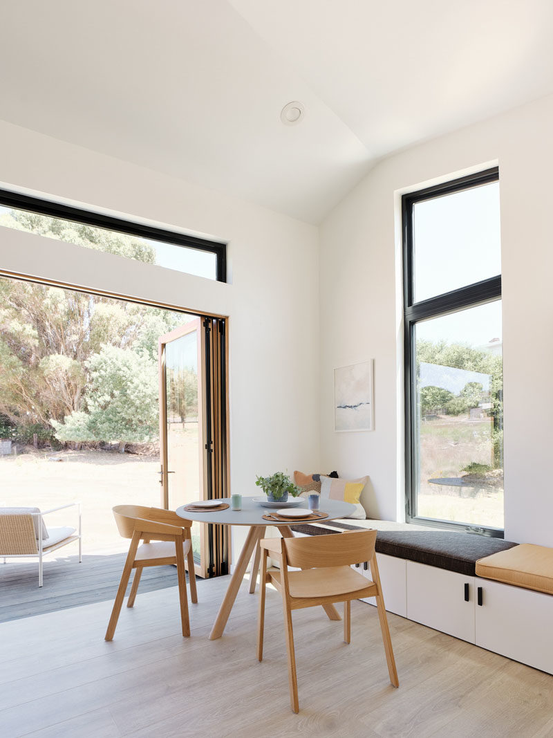 Tiny House Ideas - This modern tiny house has a 3 panel folding door that connects the interior to the outdoor space, while just inside the door is a small dining area with a bench that runs the length of the wall. #TinyHouseIdeas #ModernTinyHouse #TinyHouseDining #TinyHouseSeating