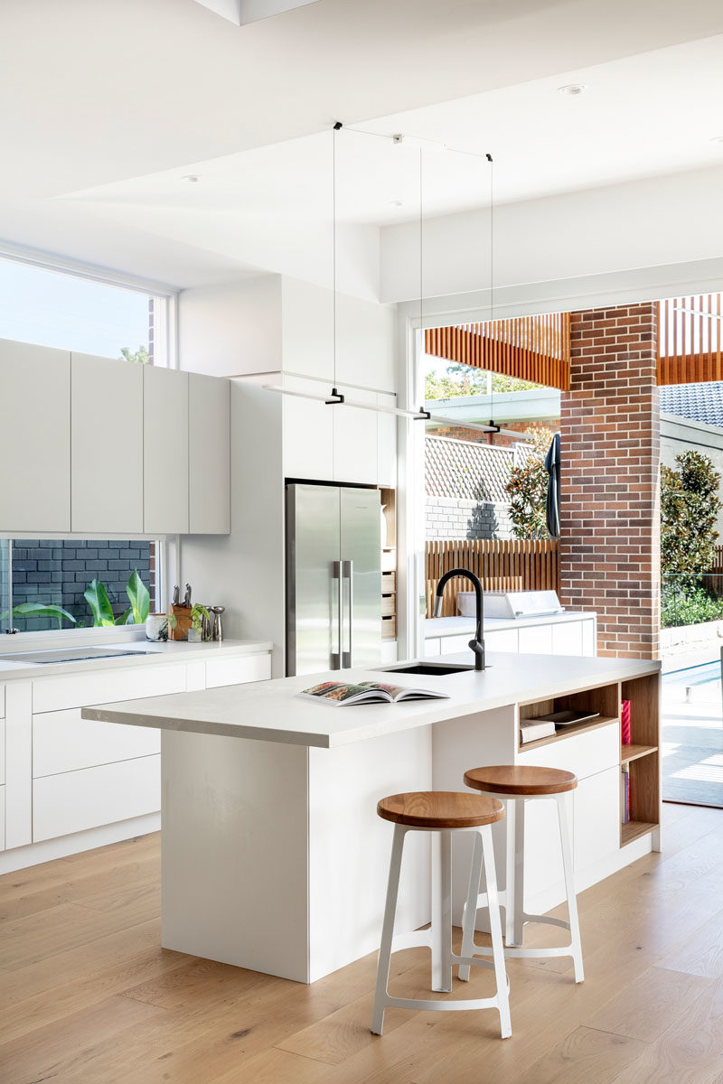 Kitchen Ideas - In this modern kitchen, minimalist white cabinets sit flush with the walls, while the island provides additional counter space and open shelving for recipe books. #KitchenIdeas #ModernKitchen #KitchenDesign #KitchenIsland