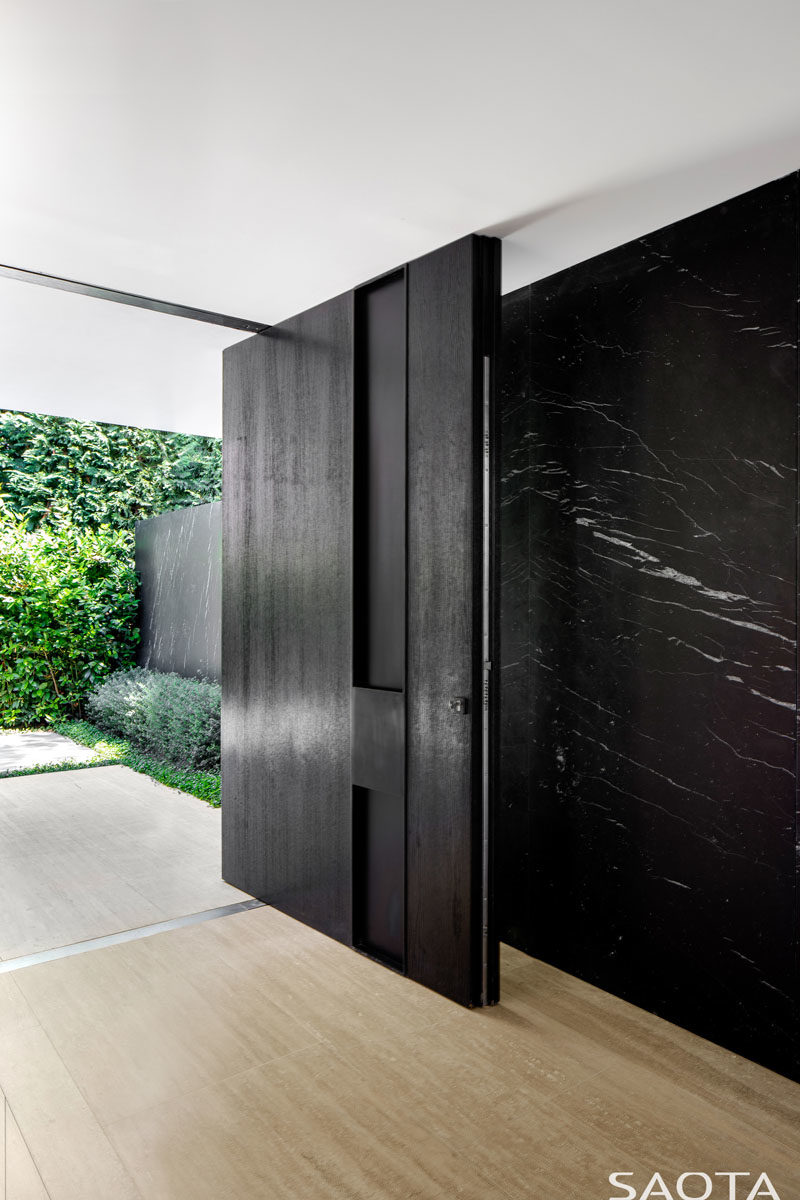 Front Door Ideas - This modern house has a large oversized black pivoting front door that opens to reveal the interior of the home, which was conceived as a gallery-like space. #FrontDoor #PivotingDoor #FrontDoorIdeas #BlackFrontDoor #PivotDoor