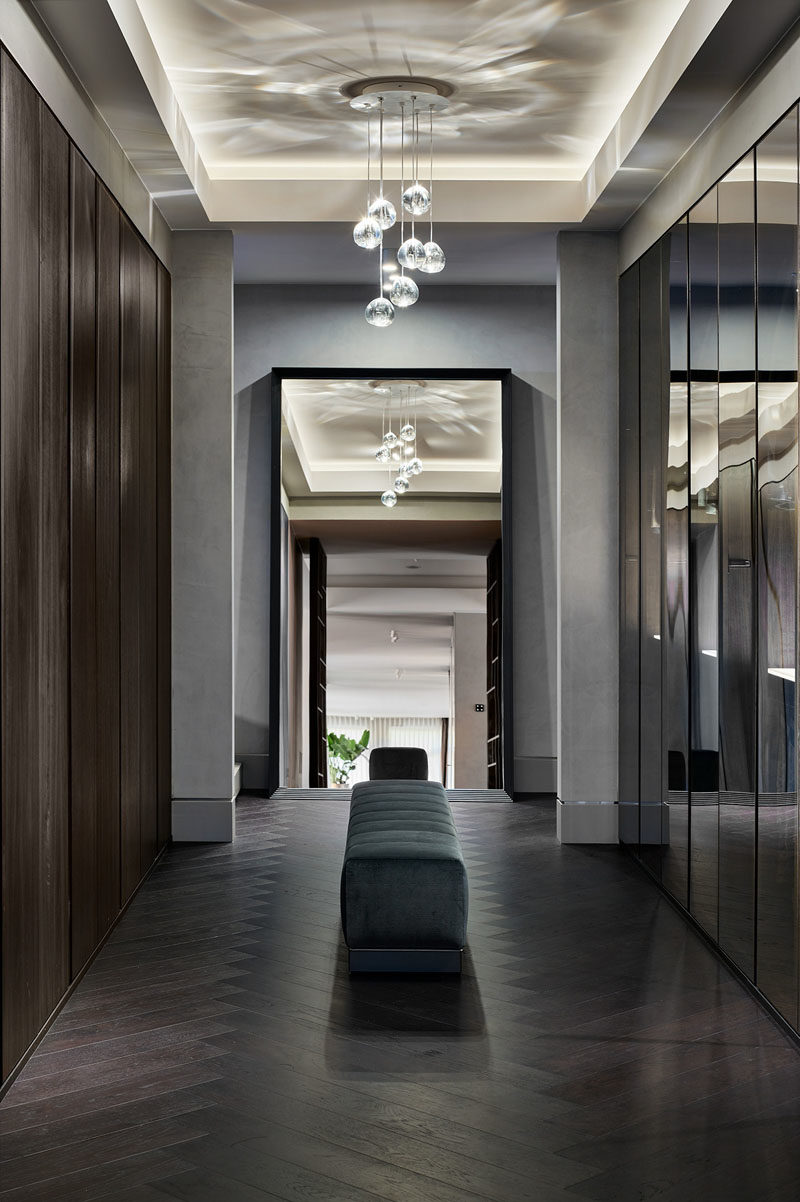 Walk-In Closet - This modern and large walk-through closet has a chandelier and mirrored closets, creating a luxurious space. The closet doors open to reveal hangers and storage space that's highlighted with hidden lighting. #ModernCloset #WalkThroughCloset #ClosetDesign