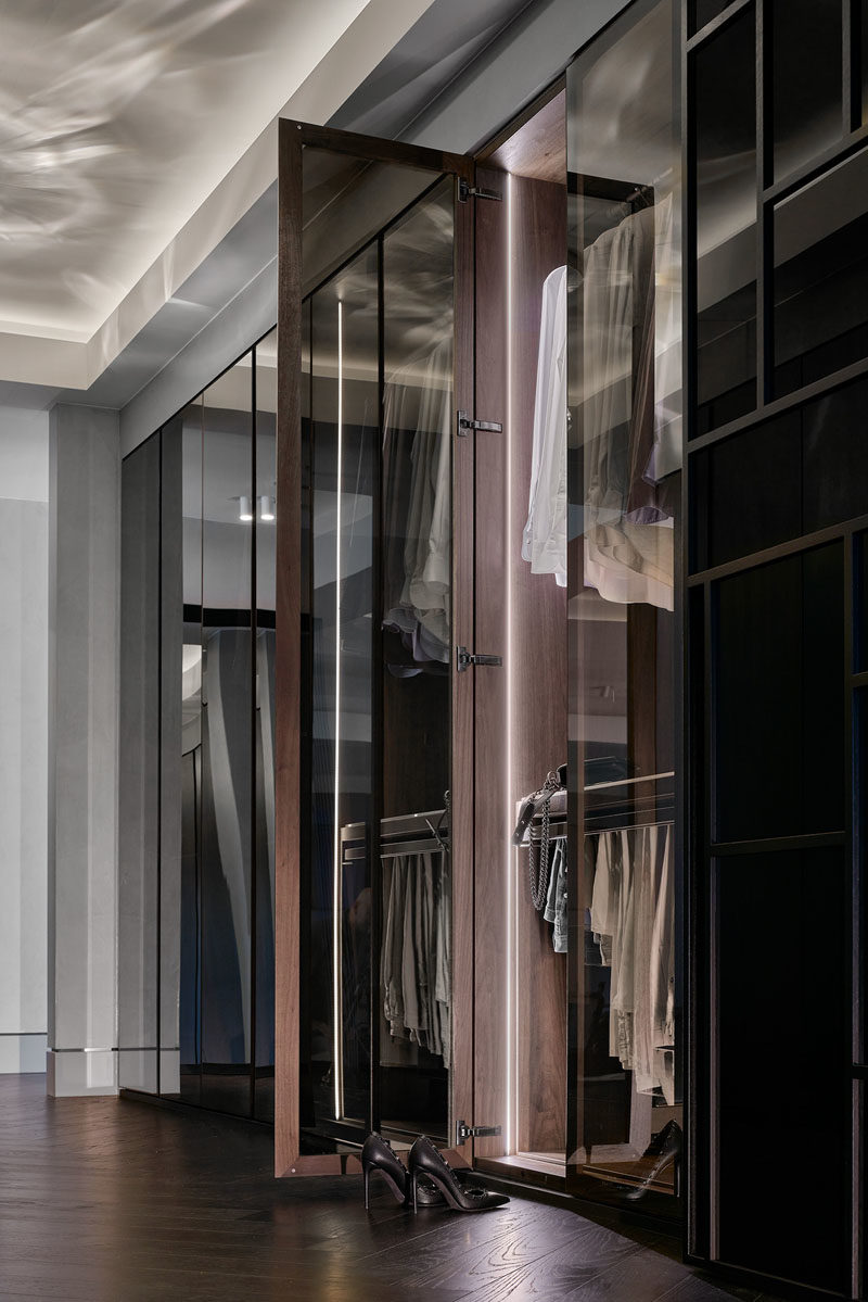 Walk-In Closet - This modern and large walk-through closet has a chandelier and mirrored closets, creating a luxurious space. The closet doors open to reveal hangers and storage space that's highlighted with hidden lighting. #ModernCloset #WalkThroughCloset #ClosetDesign
