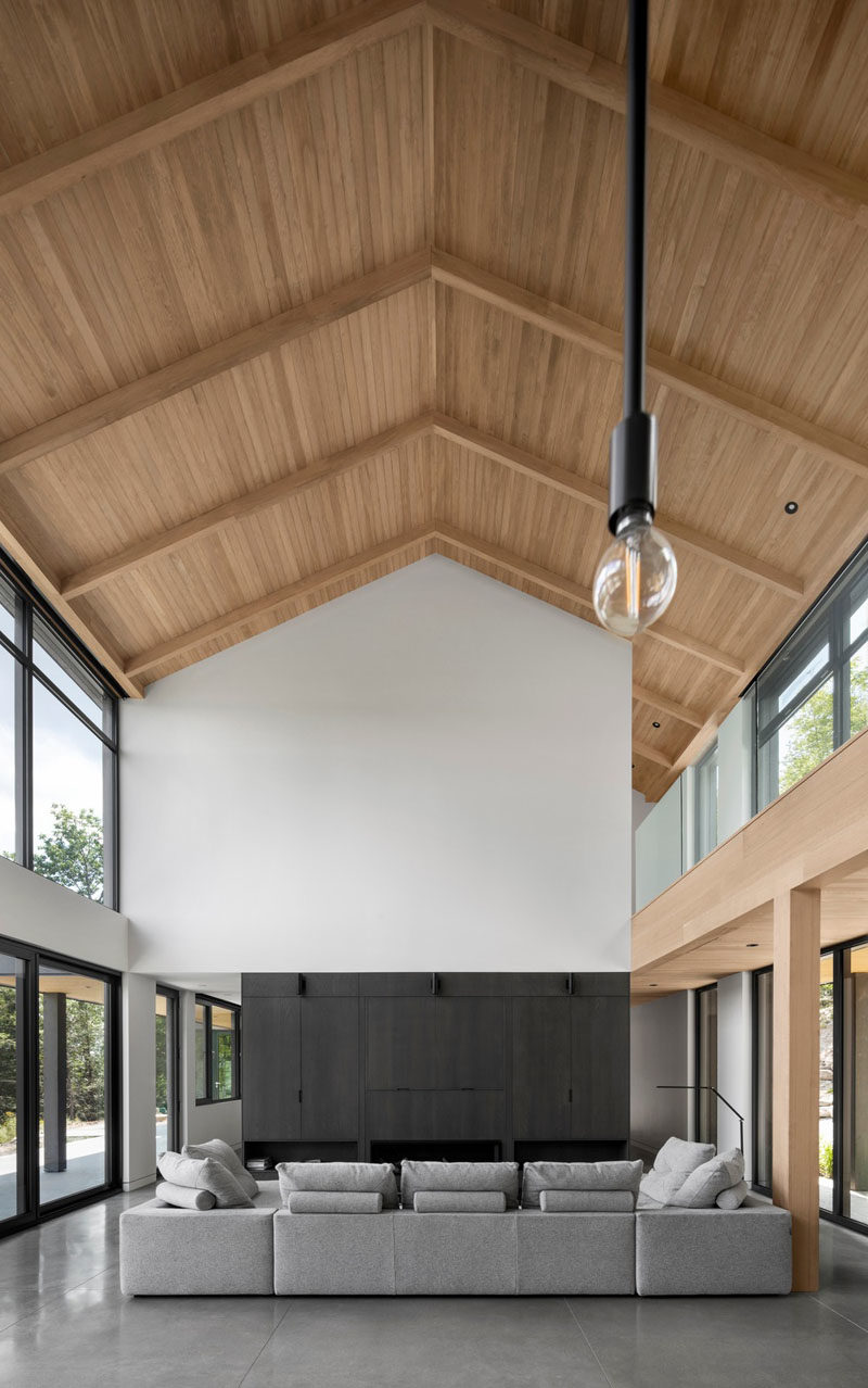 Modern Barnhouse Ideas - Inside this modern barnhouse, the gabled roof is highlighted by the wood-line ceiling that draws the eye upward. In the living room, a collection of cabinets houses the television and fireplace. #ModernBarnhouse #GabledRoof #ModernArchitecture #WoodCeiling