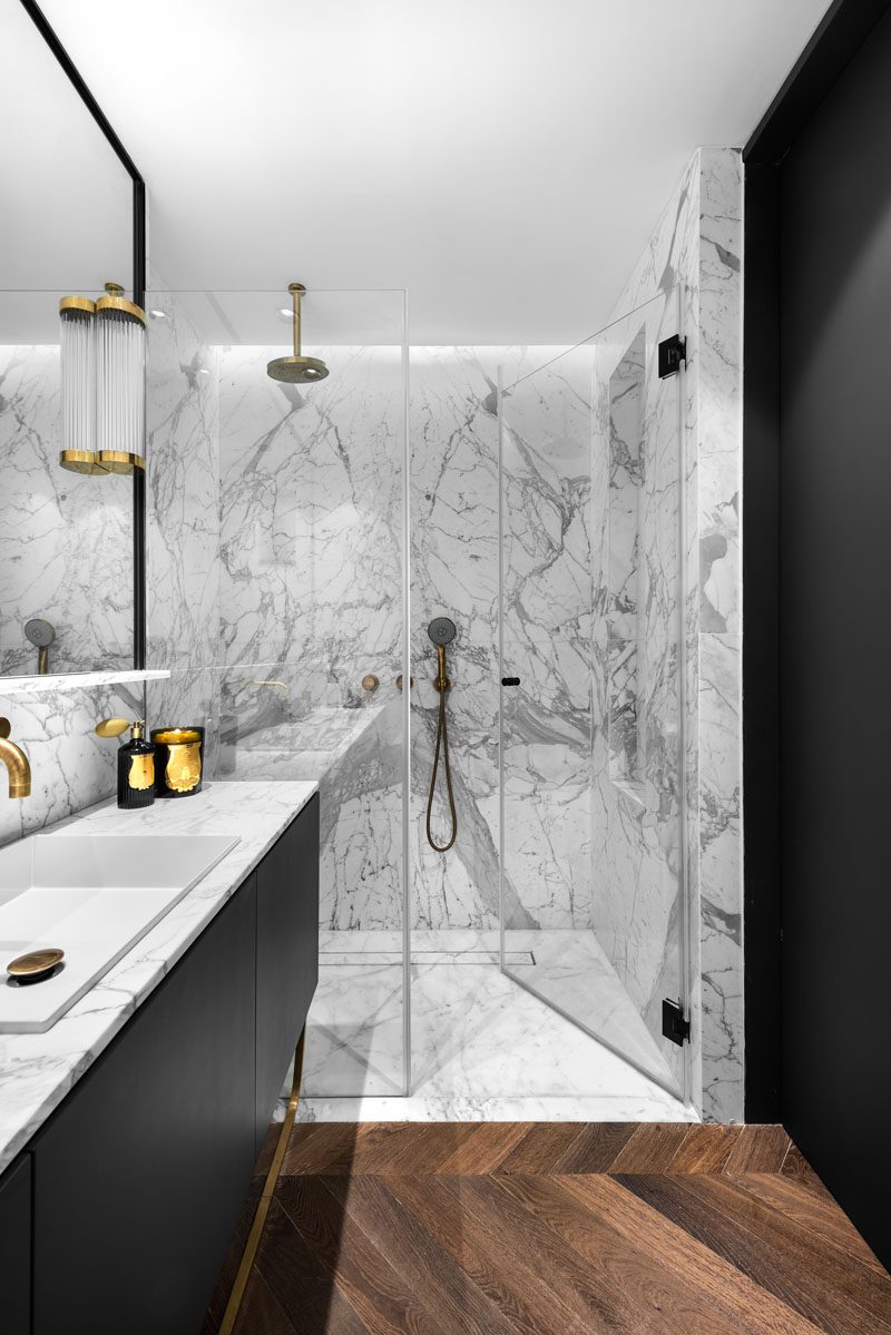 In this modern grey and black bathroom, a glass enclosed shower has hidden lighting that creates a soft glow for the space. #ModernBathroom #BathroomDesign #ShowerDesign