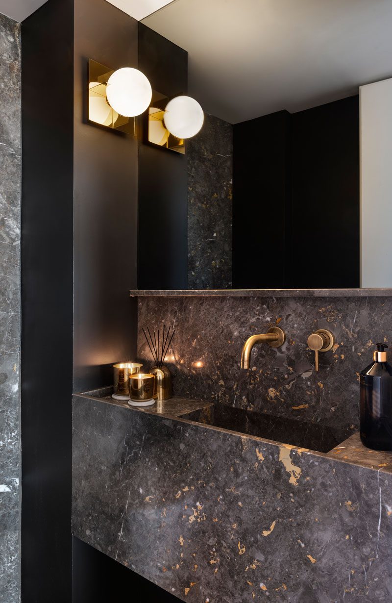 In this modern powder room, metallic accents have been paired with dark stone and black walls for a bold and dramatic appearance. #ModernPowderRoom #BathroomDesign