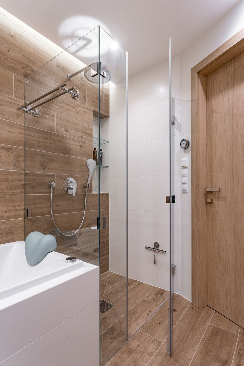 Bathroom Ideas - In the bathroom, tiles with a wood grain finish cover the wall and floor, while the glass shower surround allows light to travel throughout the small space, making it feel larger and brighter. #ModernBathroom #WoodTiles #BathroomIdeas #BathroomDesign