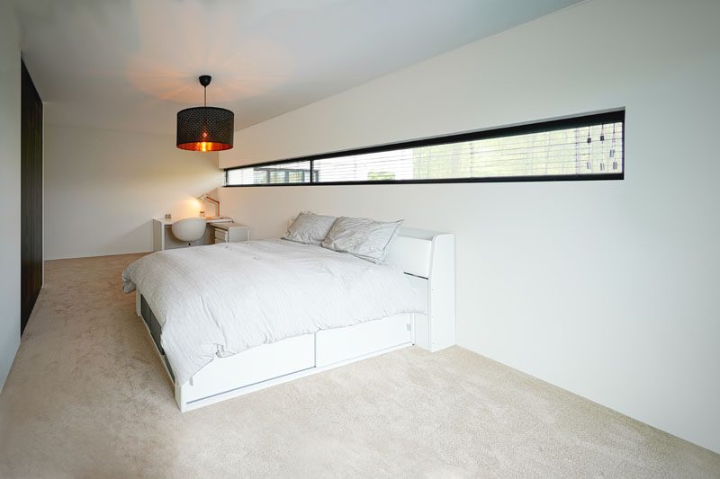 In this minimalist bedroom, a black-framed thin horizontal window runs almost the entire length of the room, and allows for natural light to filter through. #BedroomDesign #ModernBedroom #HorizontalWindow