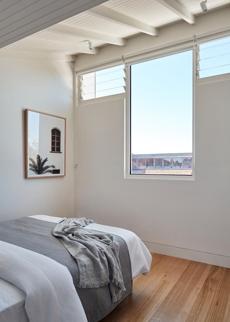 This modern bedroom has a single large window with views of the neighborhood, and is flanked by smaller louver windows, that help with air flow. #Windows #ModernWindows #Bedroom #BedroomDesign