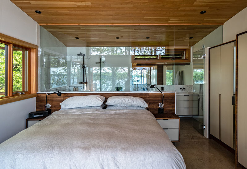 Bedroom Ideas - This modern master suite features a glass walled en-suite bathroom, maintaining the view to the lake from every part of the room, while built-in closets neatly conceal ample storage. #MasterBedroom #BedroomIdeas #EnsuiteBathroom #GlassWall