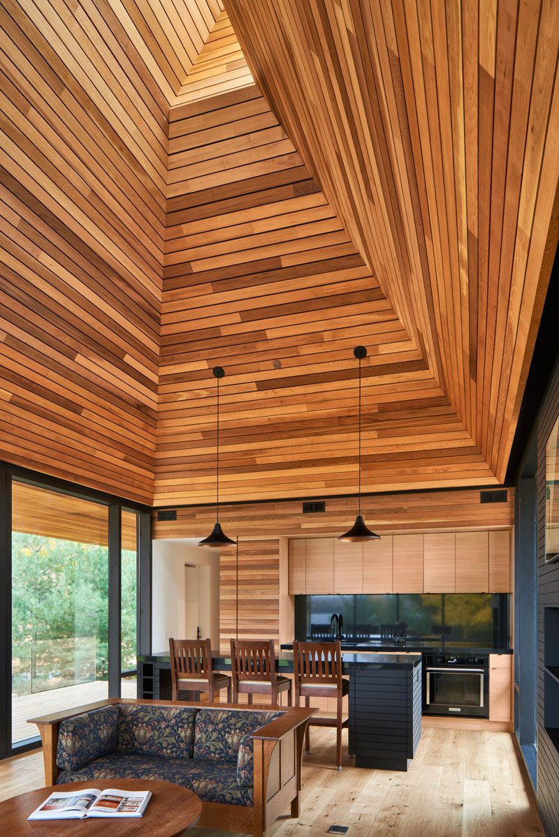 This modern cabin has an open living room and kitchen that are naturally lit from above via a periscope window in the gable. #ModernCabin #WoodCeiling #PeriscopeWindow #LivingRoom #CabinInterior