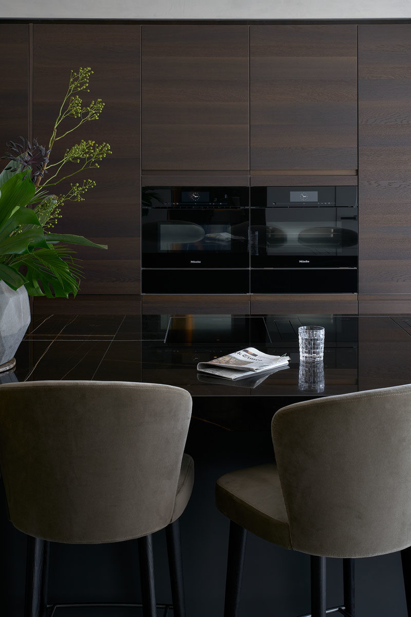 Modern Kitchen Ideas - In this modern kitchen, dark wood minimalist cabinets are complemented by black appliances and countertops. #KitchenDesign #ModernKitchen #DarkWoodKitchen