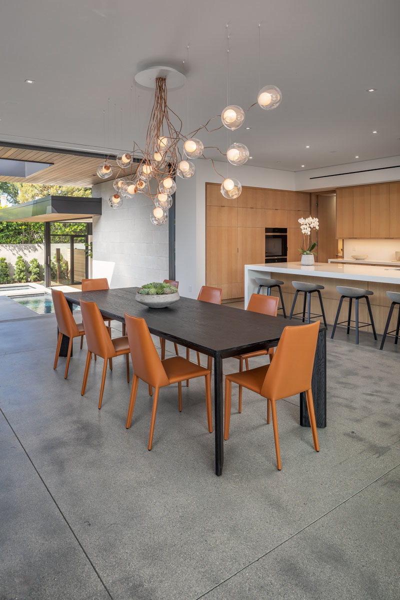 A dining table with a sculptural chandelier separates the living room and the kitchen, while polished concrete floors have used throughout this modern house.
