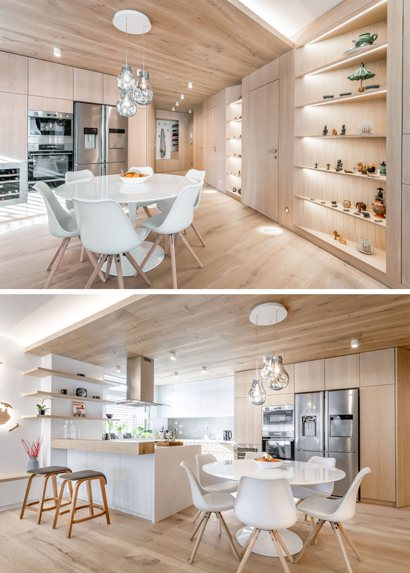 This modern apartment features built-in angled shelving that's adjacent to the dining area. Three sculptural glass pendant lights hang above the dining table, anchoring it in the open space. #ModernApartment #CustomShelving #BuiltInShelving #InteriorDesignIdeas #ApartmentIdeas #WoodLined #DiningRoomIdeas
