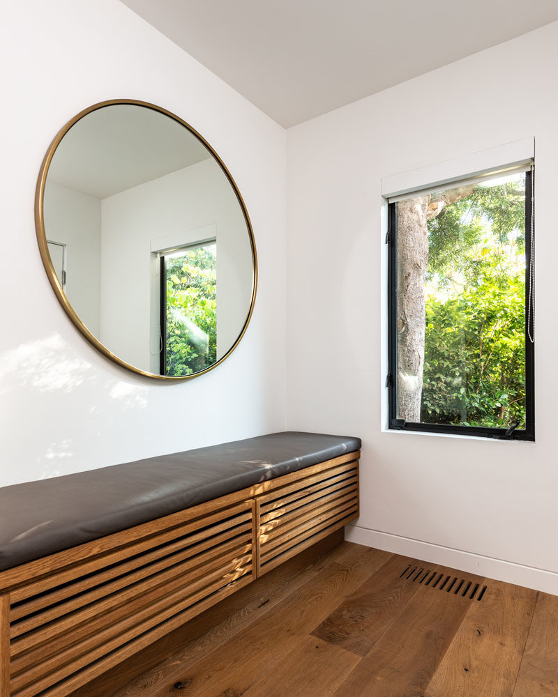 Inside this modern house, there's an entryway with a built-in wood bench that complements the European Fumed White Oak floors that are featured throughout the house. #ModernHouse #Entryway #RoundMirror #InteriorDesign #WoodFloors