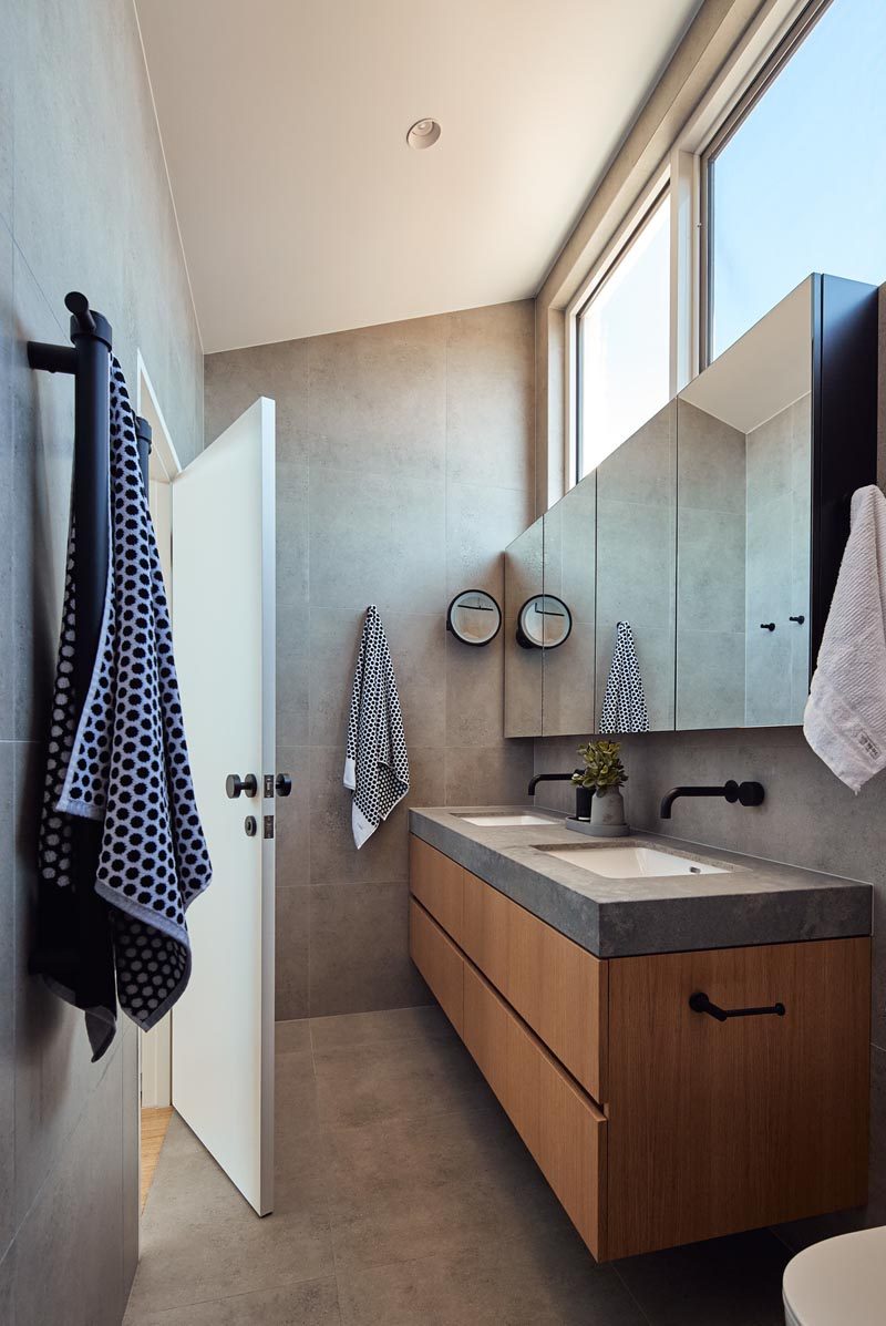 This modern en-suite bathroom has a high sloped ceiling, grey walls, and a large wall-mounted floating cabinet with a mirrored front that sits above the wood vanity. #EnsuiteBathroom #BathroomDesign #BathroomIdeas #ModernBathroom