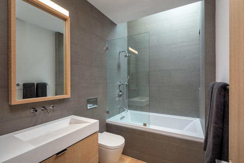 A modern bathroom with grey wall tiles, light wood accents, and a skylight.