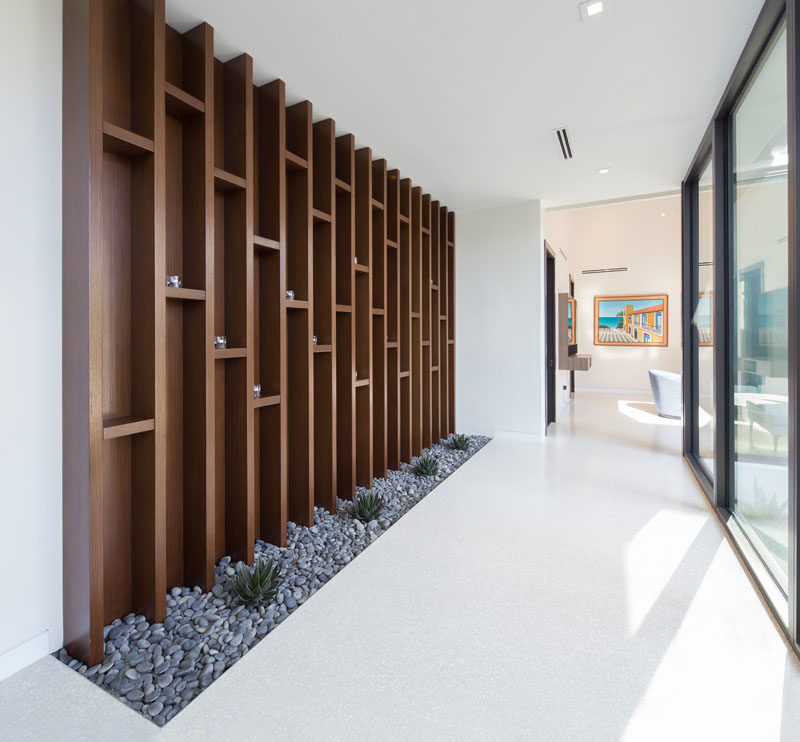 A large wood floor-to-ceiling open shelving unit in this hallway provides a place for the home owners to show off their decorative items, while the pebbles and plants at its base bring the outside in. #Shelving #Decor #InteriorDesign