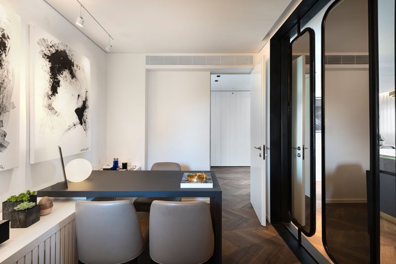 In this modern home office, there's white cabinetry that runs the length of the room, while a black desk complements the black-framed mirrored partitions and the abstract wall art. #ModernHomeOffice #HomeOfficeIdeas #MirroredPartition