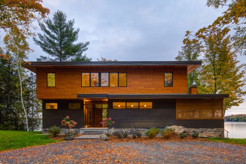 This new home was designed to take full advantage of the lake views and the landscaped spaces that surround it. Natural stone anchors the base of the cottage while dark grey and natural wood siding give the exterior a modern feel. #ModernHouse #Stone #Architecture #GreySiding #WoodSiding