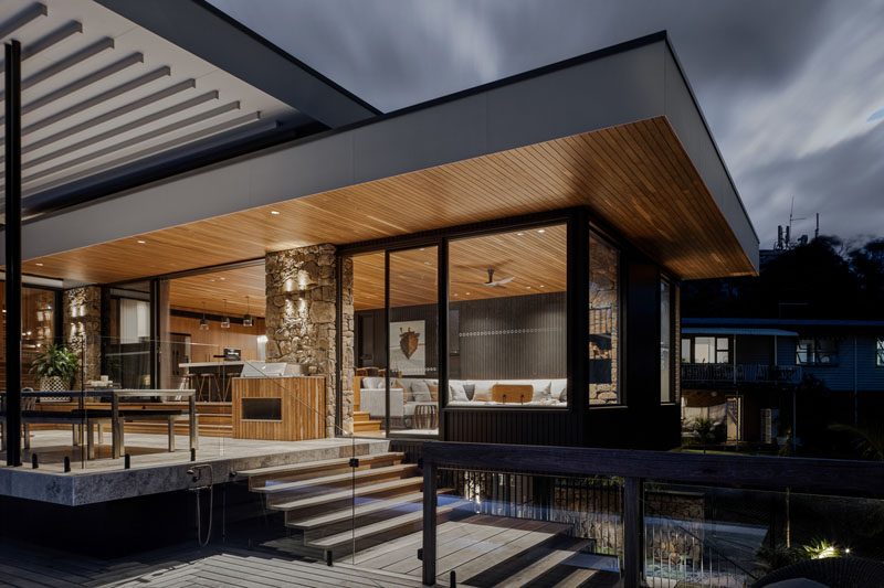 Sliding doors open the interior social spaces of this modern house, to a covered patio with steps that lead down to the backyard. #CoveredPatio #ModernHouse #WoodCeiling