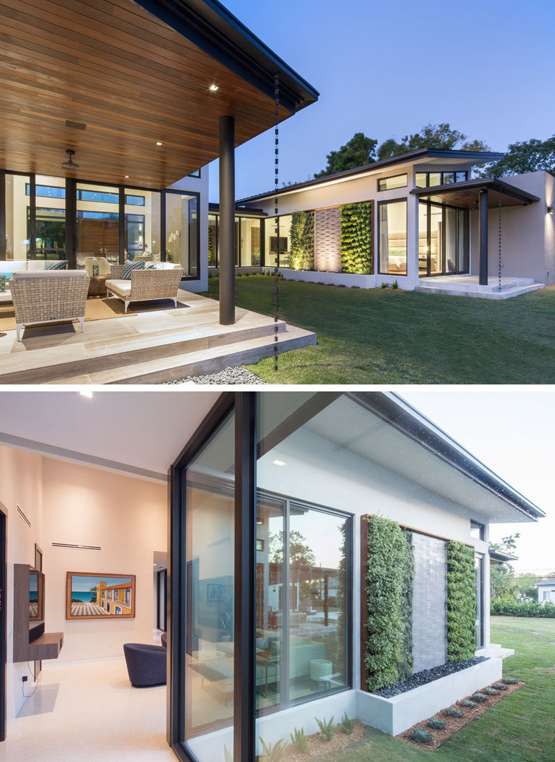 Sliding glass doors connect the interiors of this modern house with a covered outdoor space and the backyard. A rainwater chain adds a little decorative touch, and a water feature with plant walls and hidden lighting creates a focal point. #Backyard #YardIdeas #OutdoorLounge #WaterFeature #Landscaping