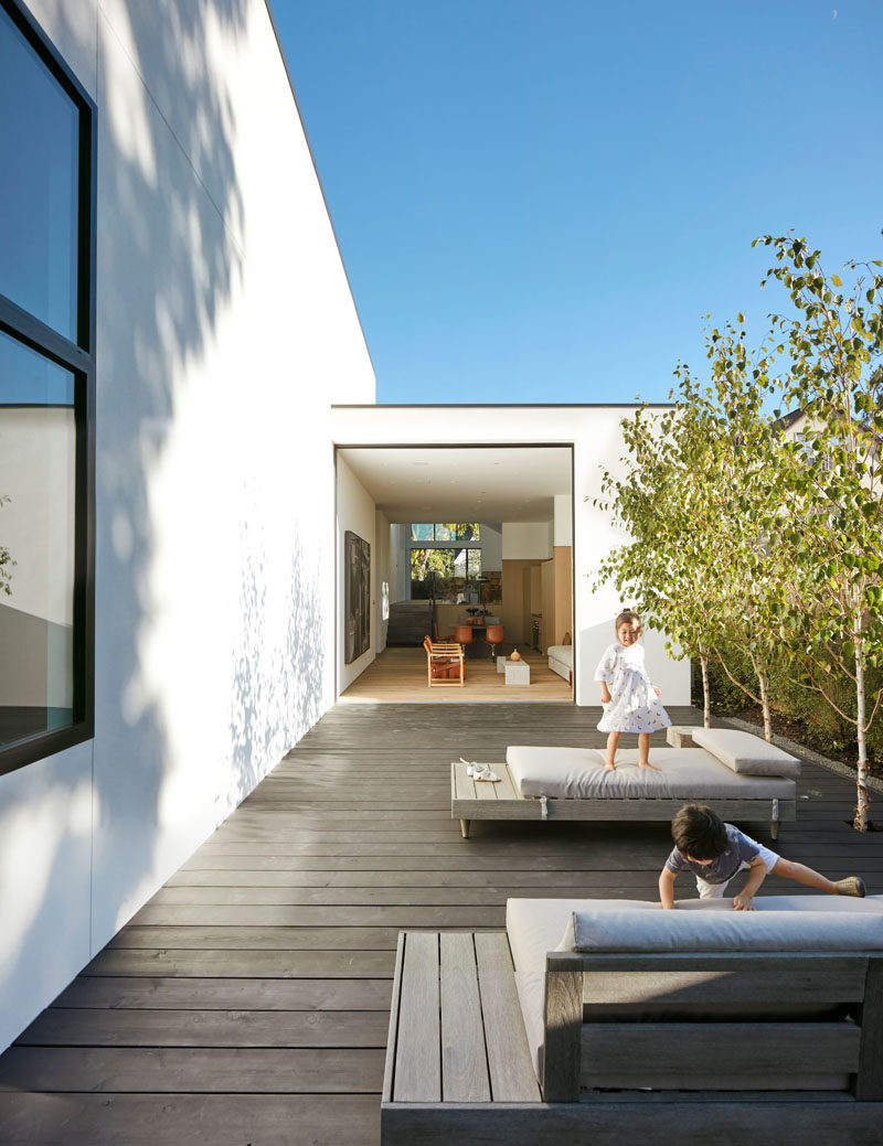 This modern house has a courtyard that features dark wood decking lined with trees and a couple of comfortable daybeds. #Courtyard #CourtyardDesign