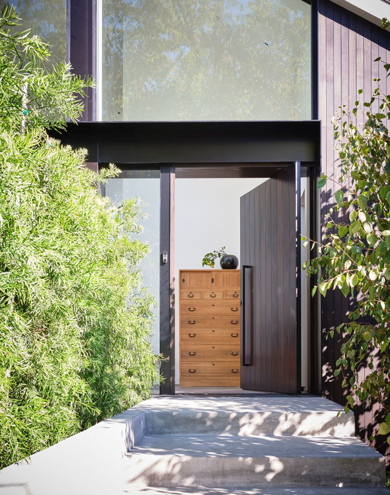 A pivoting dark wood front door welcomes visitors to this modern house. #FrontDoor #WoodFrontDoor #PivotingFrontDoor