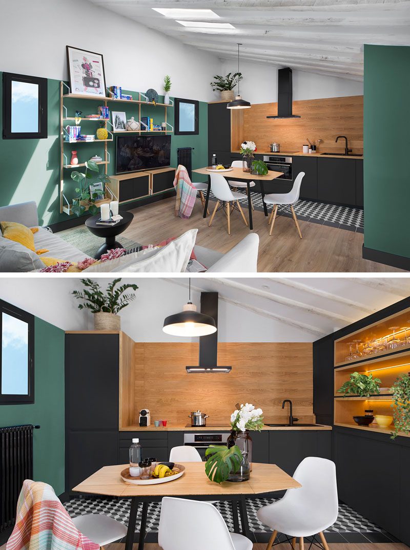 In this modern apartment, a wall shelf adds storage, while matte black kitchen cabinets complement the thick black window frames. Wood-lined shelving in the kitchen has hidden lighting that adds a soft glow to the space and highlights the glassware. #ModernApartment #DiningArea #Shelving #MatteBlackKitchen #KitchenDesign #Shelving