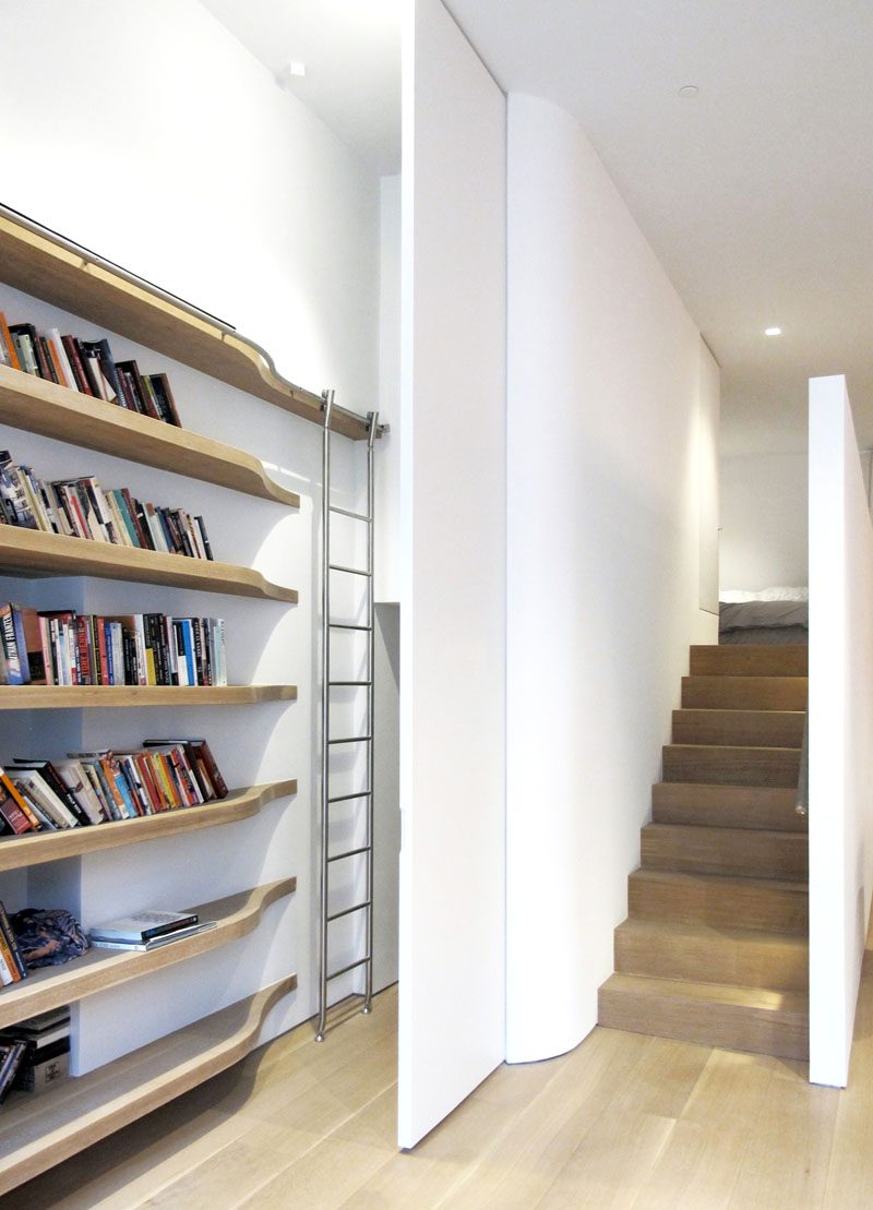 A custom stainless steel telescoping ladder and curving track follow the curving solid oak shelves and allow the ladder to be rolled out of sight behind a full height flush door to the laundry, storage, and mechanical room beneath the mezzanine. #ShelvingDesign #ShelvingIdeas #Stairs