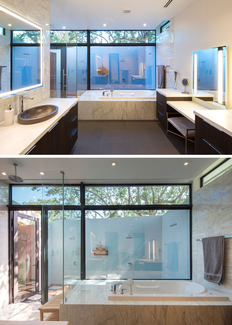 In this modern master bathroom, dark wood vanities provide a rich element to the space, while the built-in bath has views of the outdoor showers that are accessible via the interior shower. Carrara marble, mirrors with lighting, and large windows have been used to keep the bathroom bright. #BathroomIdeas #MasterBathroom #OutdoorShower #BuiltInBathtub #WoodVanity