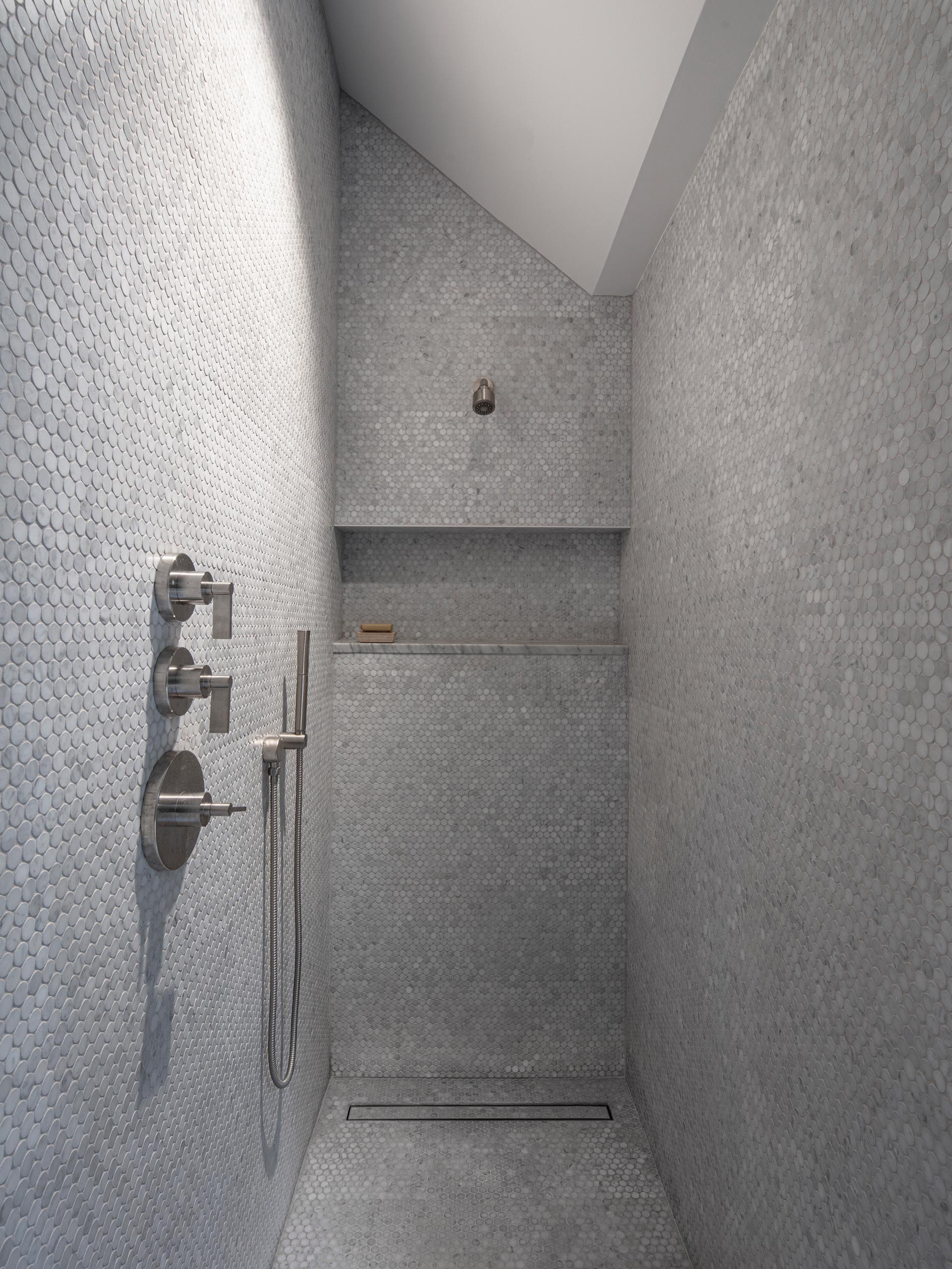 A modern shower with floor-to-ceiling grey penny tiles, a linear shower drain, and a built-in shelf.