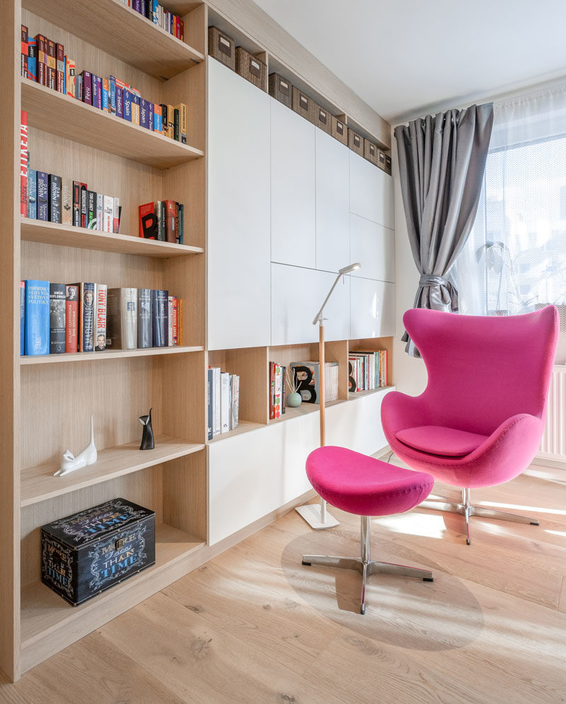 Library Ideas - This modern apartment has a small library area, with bookshelves and a bright pink armchair. #HomeLibrary #ReadingCorner #LibraryIdeas #ShelvingIdeas