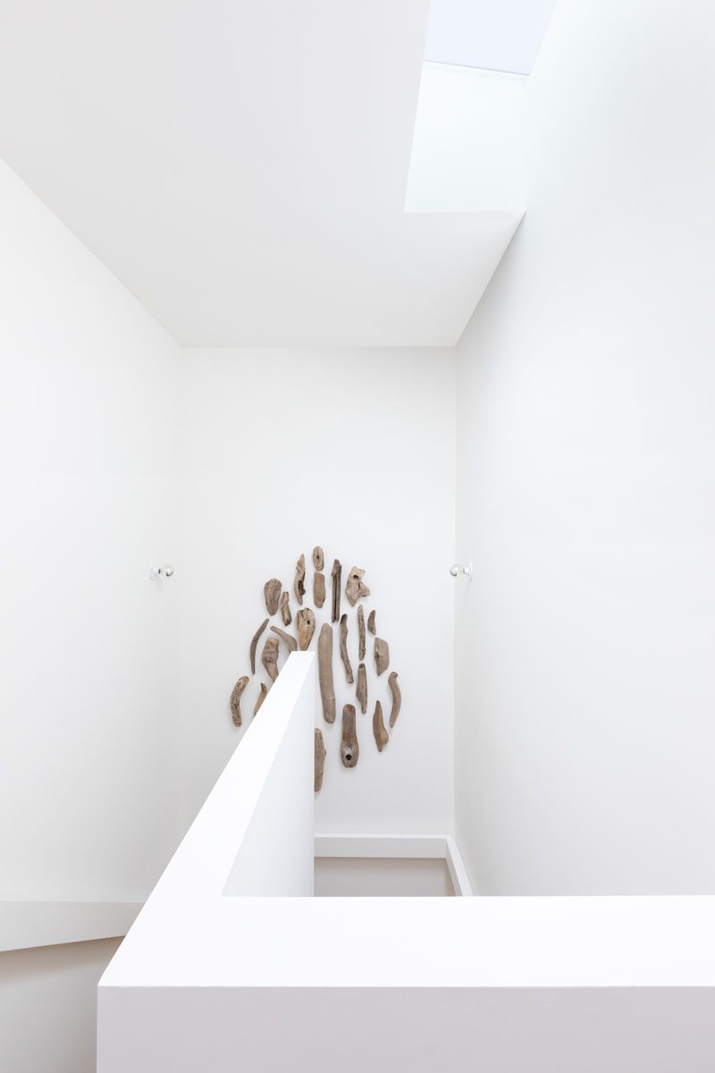 A staircase leads to the second floor of this modern house and is lit by a skylight, while driftwood artwork provides a focal point in the space. #ModernStairs #WhiteStairs #DriftwoodArt #Skylight