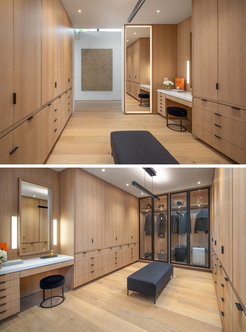 A large walk-in closet has a floor-to-ceiling mirror framed by soft lighting, a vanity area, a glass enclosed wardrobe, and plenty of cabinets and drawers for clothing storage.