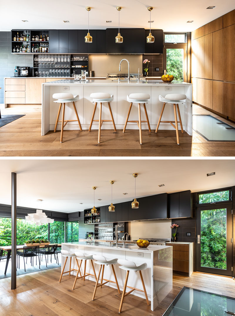In this modern kitchen, there's hidden wine storage, and a large white island with a group of Artek Golden Bell lighting adding a touch of glam. #ModernKitchen #KitchenIsland #KitchenDesign