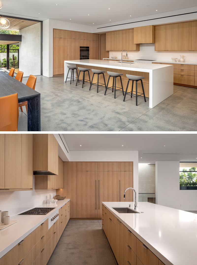 A modern gourmet kitchen with minimalist wood cabinets, an integrated fridge, a large white island with seating, and a walk-in pantry.