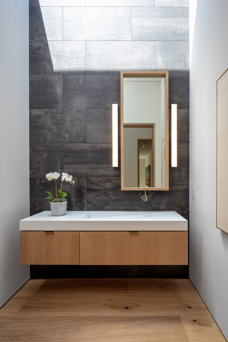 Vanity Ideas - In this modern bathroom, grey tiles provide a backdrop for the floating wood vanity, that features a sink integrated into the countertop. #BathroomIdeas #BathroomVanity #ModernBathroom