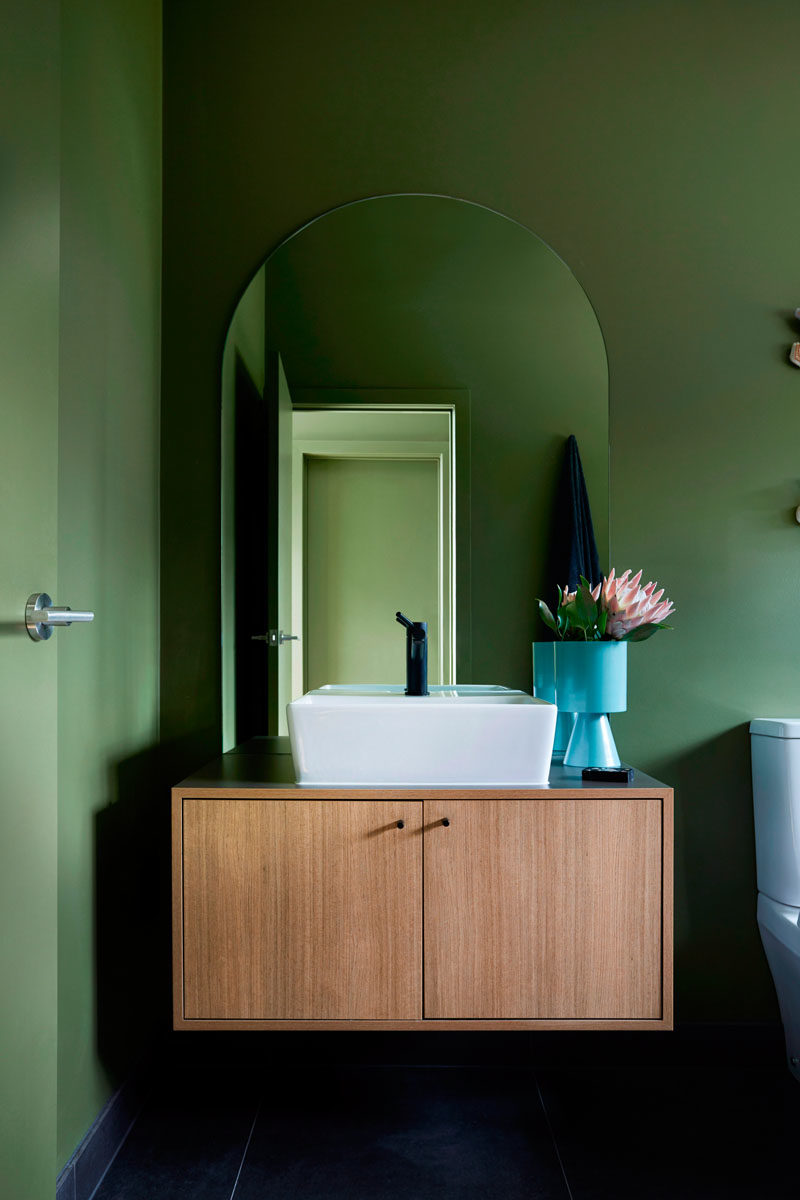 In this modern bathroom, a floating wood vanity sits below an arched mirror, while a vase adds a pop of bright blue. #BathroomDesign #ModernBathroom