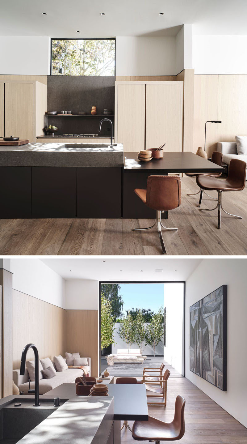 In this modern kitchen, light wood cabinets match the wood wall accent, while the dark island drops downs to form a secondary dining area. #KitchenDesign #ModernKitchen #WoodKitchen