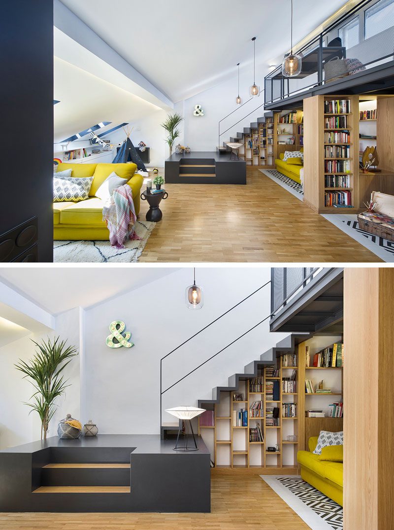 In this modern attic, stairs provide separation between the living room and a small library area that features shelving that neatly fits beneath the stairs and mezzanine. #AtticRenovation #ModernAttic #AtticDesign