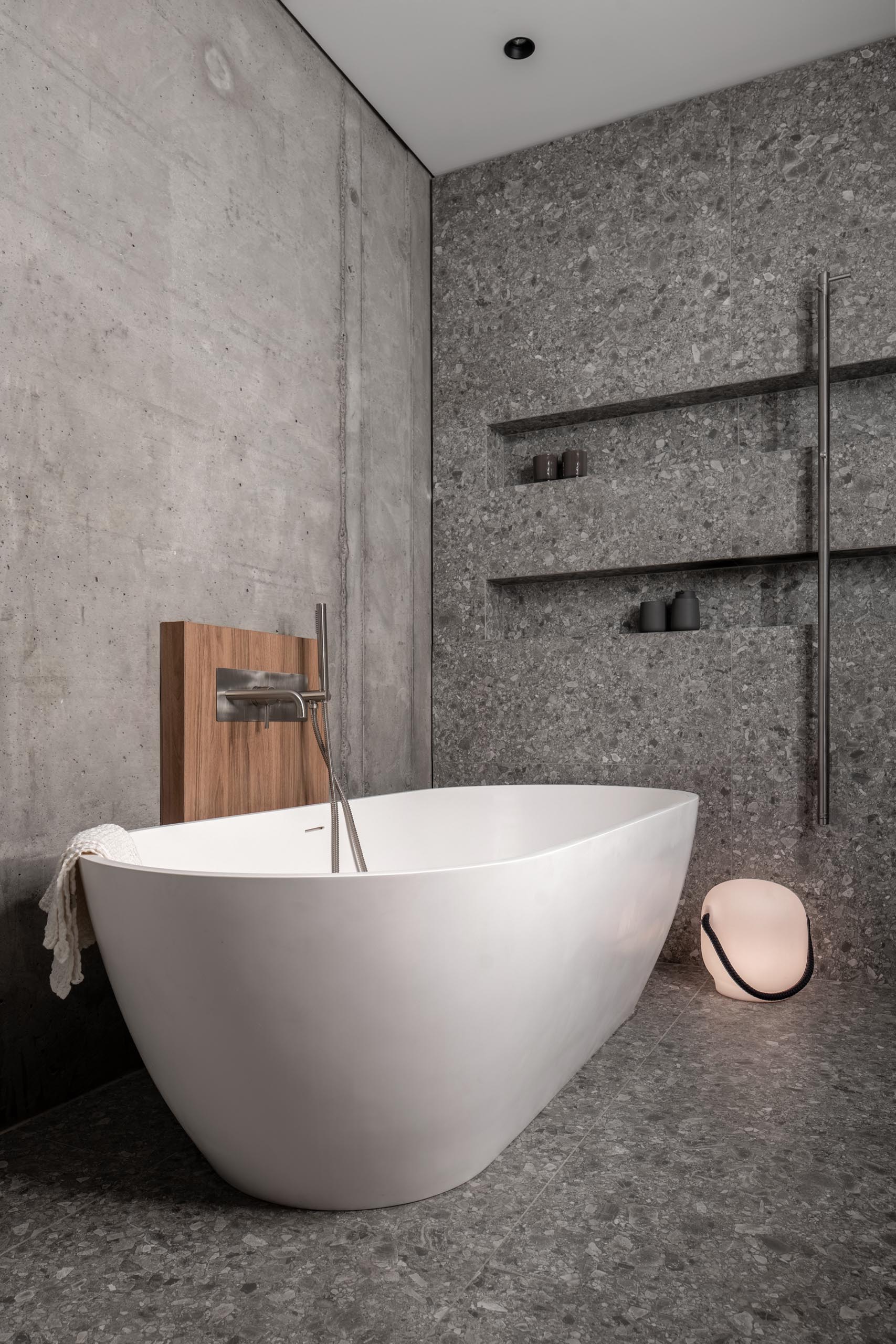 A modern grey bathroom with two shower niches, and a freestanding white bathtub.