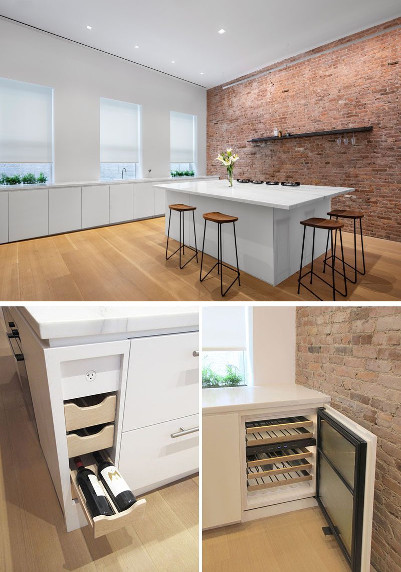 The new kitchen takes full advantage of the morning light, with planters set on each side of a custom height faucet that rises from behind the stone counter. Appliances and functions have all been concealed, while flush mounted hobs are set into the counter of the island, that features a pop-up downdraft vent that disappears when not in use. #WhiteKitchen #MinimalistKitchen #KitchenDesign #KitchenIsland