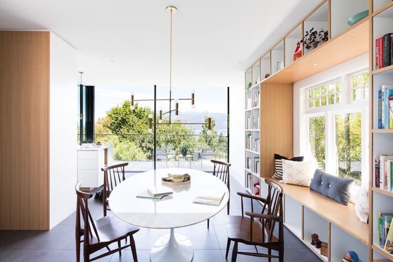 This modern house has a wood framed built-in window seat that's surrounded by open shelving, creating places to store books, decorative items, and toys. #WindowSeat #Shelving #InteriorDesign #DiningRoom