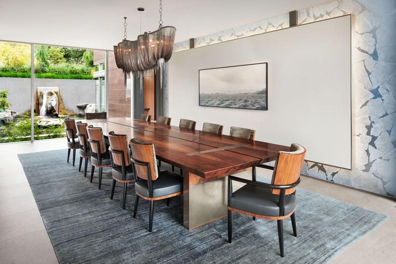 This modern dining room showcases statement pieces like a large dining table, a sculptural light, a backlit wall, and artwork. #DiningRoom #Art #ModernInterior